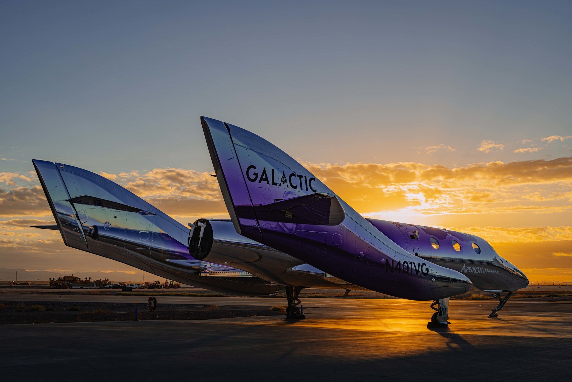 Virgin Galactic's new spaceship, its purple and chrome tail booms marked GALACTIC and its nose marked Apeiron and N401VG, parked on a runway in low sun.